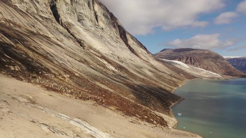 Slow and majestic aerial drone ascending view of the Sam Ford Fjord, Canada, near Greenland, with ice and rock cliffs rising steeply from the shore, with high details of the harsh ground