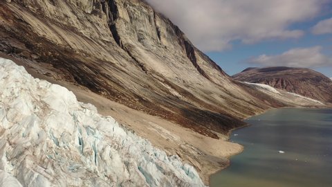 Slow and majestic aerial drone dolly view of the Sam Ford Fjord, Canada, near Greenland, with ice and rock cliffs rising steeply from the shore, with high details of the harsh ground