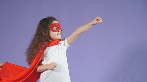 Positive little girl enthusiastically raised arms up, dressed in red mask and red cloak. Spaceman concept