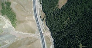 aerial bird's eye of xinjiang highway cars running between forest and mountains in nature 4k landscape drone footage