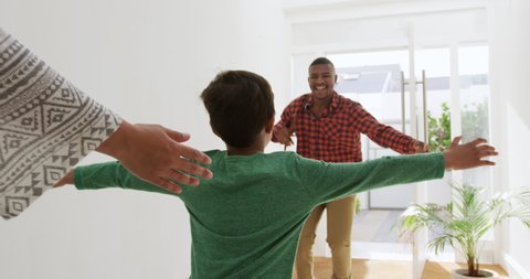 Rear view of a mother and her young mixed race son greeting his African American father as he arrives home, the son running to greet him in the sunlit corridor, slow motion