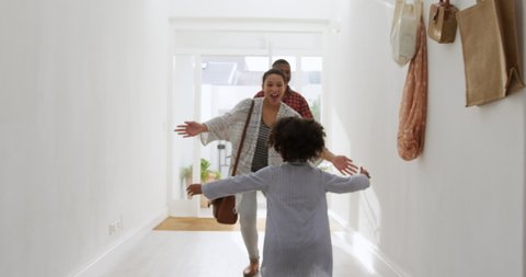 Rear view of a young African American girl running to greet her parents and embracing them in the sunlit corridor as they arrive home, slow motion