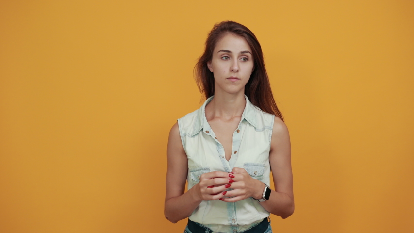 Young woman in blue denim shirt keeping hands up, looking pretty isolated on orange background in studio. People sincere emotions, lifestyle concept.