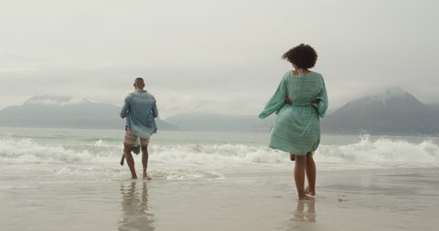 Side view of an African American couple on a beach by the sea, holding hands with their young son and daughter and spinning them around, slow motion