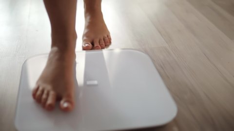 Woman On Scales Measure Weight.Human Barefoot Measuring Body Fat Overweight.Girl Legs Step On Bathroom Scale.Close Up Woman Checking BMI Weight Loss.Diet Female Feet Standing Weighing Scales On Room