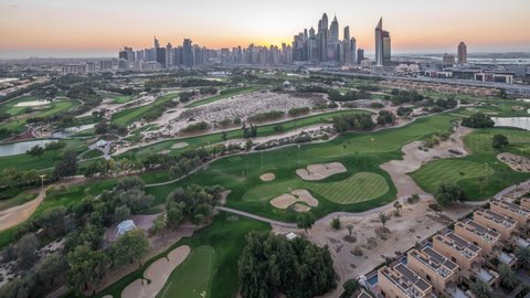 Jumeirah lake towers and Dubai Marina skyscrapers and golf course day to night transition timelapse, Dubai, United Arab Emirates. Aerial view from Greens district after sunset