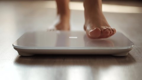 Human Barefoot Measuring Body Fat Overweight.Girl Legs Step On Bathroom Scale.Woman On Scales Measure Weight.Close Up Woman Checking BMI Weight Loss.Diet Female Feet Standing Weighing Scales On Room