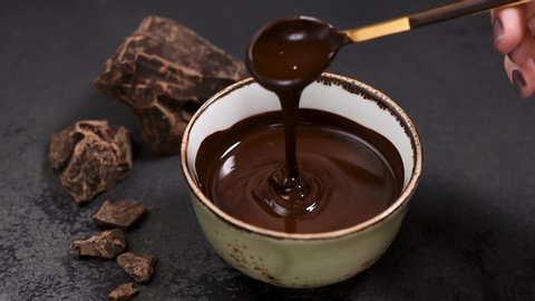 Liquid dark chocolate in bowl. Female hand mixing melted dark chocolate with spoon. Chocolate fondue