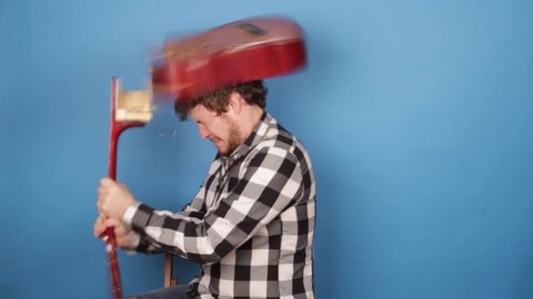 A mad man hits himself on the head with a guitar. The guy breaks a guitar on his head on a blue background.