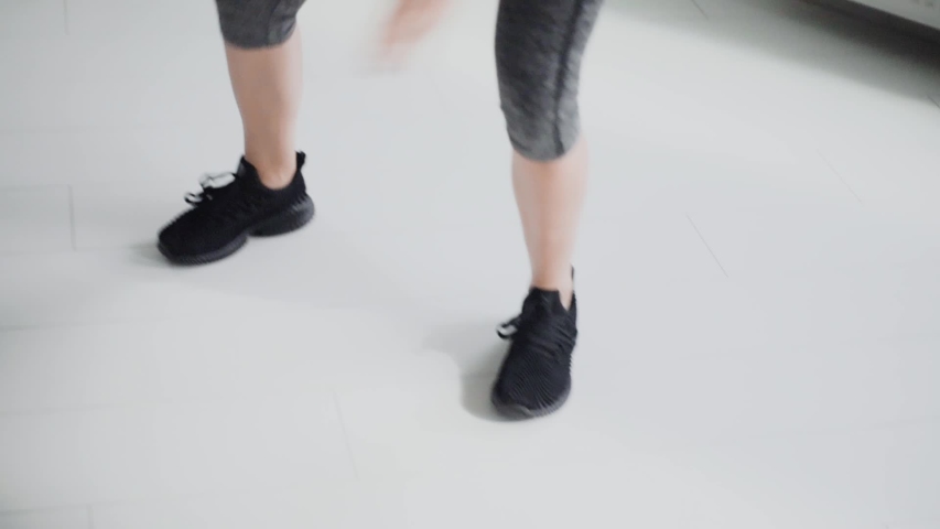 closeup on sportswoman legs making sport exercizes. young fit girl in gray leggings, black sneakers exercising at gym. female makes jumps, squats, side steps. healthy lifestyle, fitness, weight loss