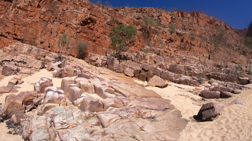 Crossing the dry creek bed with high cliffs during Ormiston Pound walk, a popular circular walk. West MacDonnell Ranges in Northern Territory, Central Australia Outback.