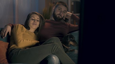 Tired bored couple relaxing on the sofa with their dog and watching TV shows