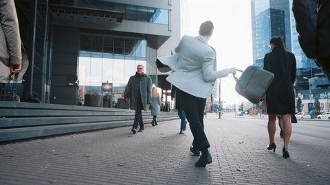 Cheerful Young Businessman in a Grey Blazer is Actively Dancing on a City Street. Office Manager Moves Through Busy Office Crowds Commuting to Work. He's Holding a Leather Case.