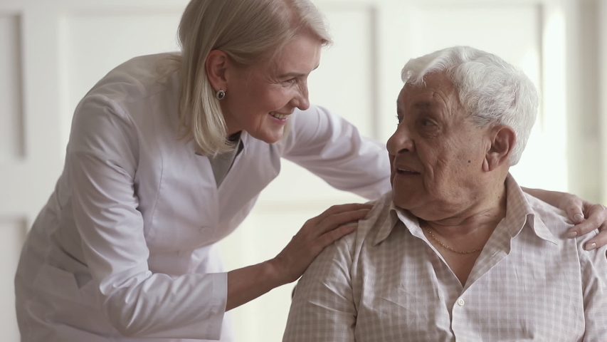 Pleasant friendly middle aged nurse embracing shoulders of 80s male pensioner. Smiling female general practitioner comforting communicating with happy retired patient, asking about health condition. | Shutterstock HD Video #1042130740