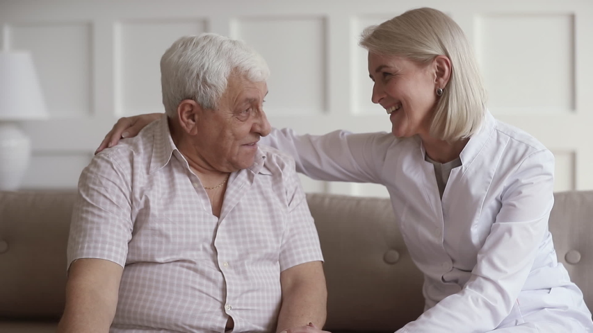Smiling middle aged nurse embracing shoulders of happy 80s male patient, communicating at home. Pleasant mature kind female general practitioner talking chatting with elderly man during checkup. | Shutterstock HD Video #1042130758