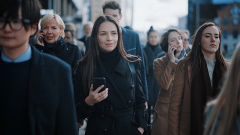 Beautiful Businesswoman in Black Coat is Using a Smartphone on a Street in Downtown. She Walks on a Crowded Pedestrian Street and Looks Successful. She Dials a Number and Talks on Mobile.