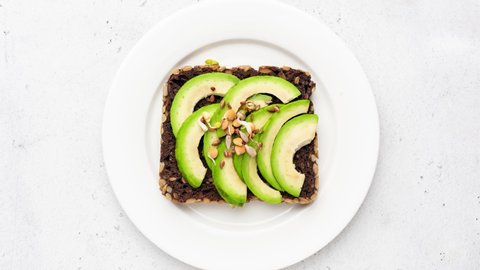 Stop motion animation of eating rye bread and avocado, healthy toast with sprouts and seeds. Top view