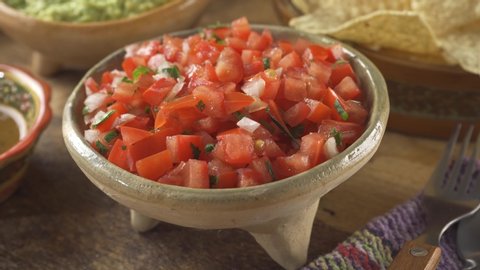 A bowl of freshly made salsa pico de gallo on a rustic wood table top.
