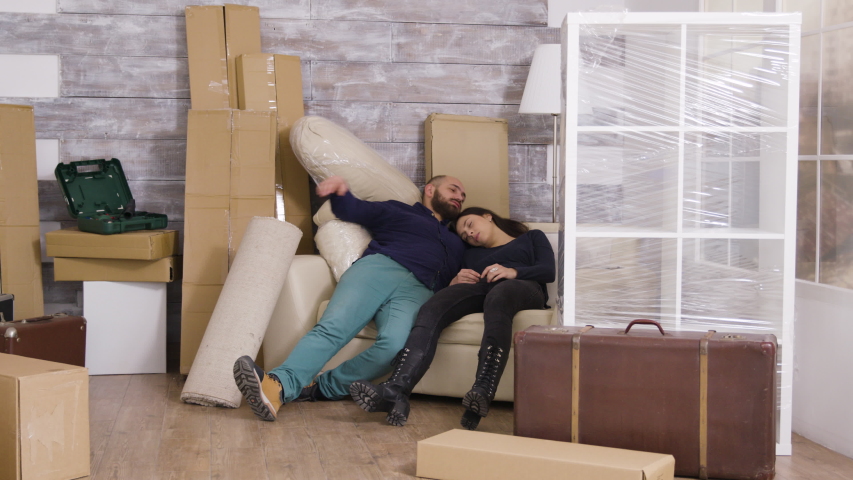 Tired young couple after carrying boxes in their new apartment and crashing on the sofa. | Shutterstock HD Video #1042145650