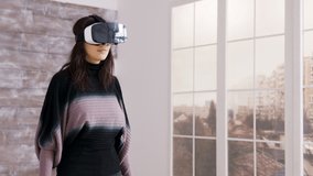 Beautiful female home designer using virtual reality goggles inside of an empty apartment.