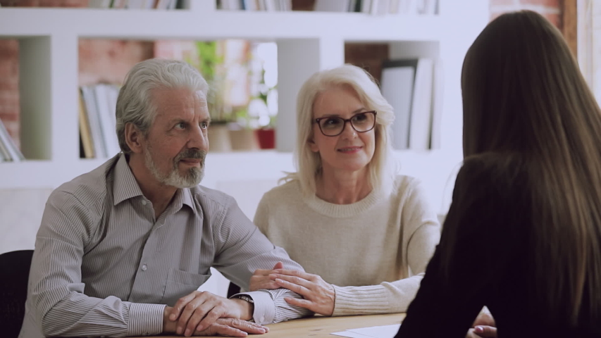 Happy middle aged family couple meeting female real estate agent, financial advisor or lawyer, discussing contract details, making agreement at office. Satisfied client shaking hands with saleswoman. Royalty-Free Stock Footage #1042151323