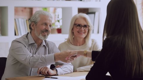Happy middle aged family couple meeting female real estate agent, financial advisor or lawyer, discussing contract details, making agreement at office. Satisfied client shaking hands with saleswoman.