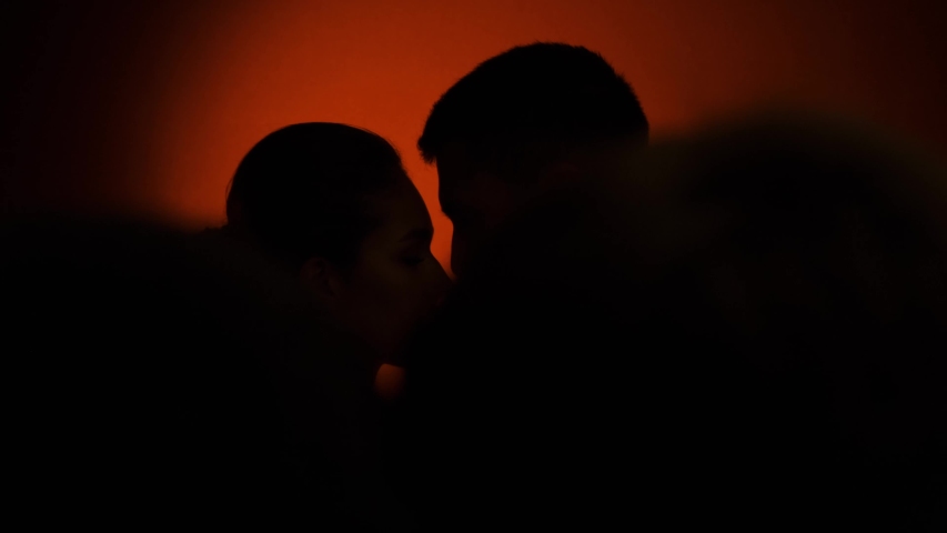 Silhouettes of beautiful young couple in wedding suits side by side.  Dark red background. Love story. Slow motion 4K