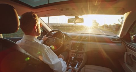 Fashionable retired business man driving car towards bright scenery sun pleasure shining over the road. Elegant male driver traveling by automobile. Enjoying sunset sky. Freedom inspire. Future coming