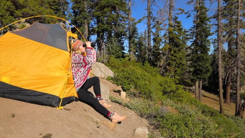 The view of the Yosemite Valley from a mountain path on a hillside.A yellow tent stands on the trail. A girl sits at the edge of a tent and watches the valley through binoculars.Yosemite National Park