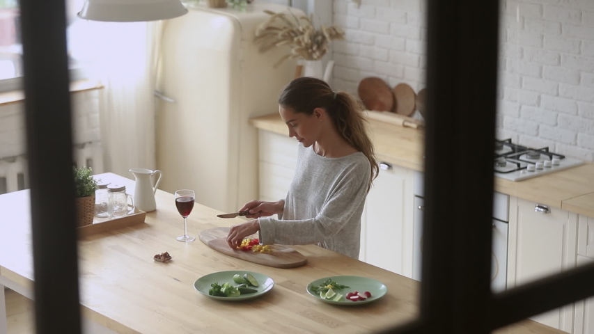 Top view young smiling mixed race woman standing at countertop, chopping vegetables in modern kitchen. Positive millennial lady preparing food alone at home, dreaming about romantic evening. Royalty-Free Stock Footage #1042155751