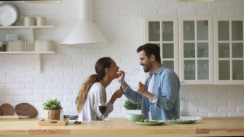 Overjoyed young married spouse using different kitchenware as microphones, pretending to be singers. Excited happy mixed race family couple dancing to favorite music, singing song as duo in kitchen. Royalty-Free Stock Footage #1042155847
