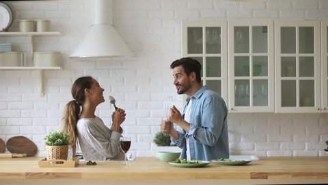 Overjoyed young married spouse using different kitchenware as microphones, pretending to be singers. Excited happy mixed race family couple dancing to favorite music, singing song as duo in kitchen.