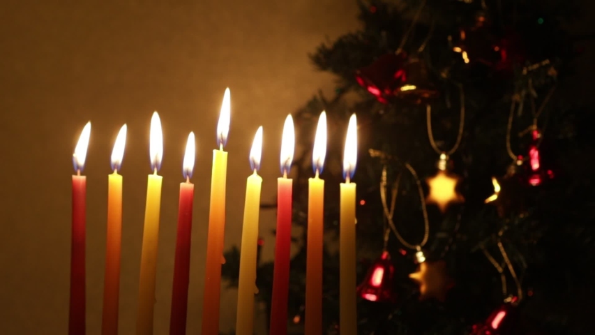 Loop - Hanukkah candles in front of Christmas tree with lights going on and off. The tree is decorated with Christmas bells and stars of David. Concept of two simultaneously happening holidays
