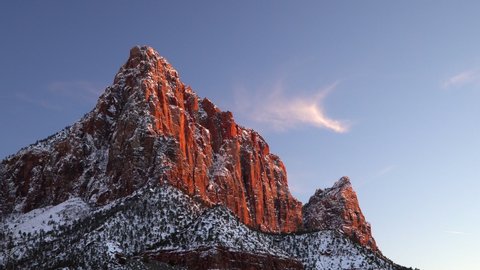 View of The Watchman as its cliff face is glowing at sunset in winter moving past trees in Zion National Park.