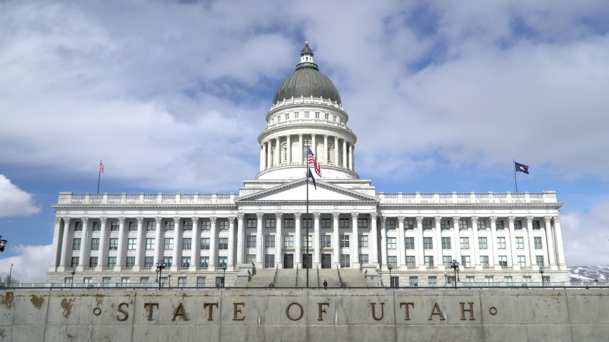 View of the Utah Capitol Building as flags are waving against sky with big fluffy clouds.