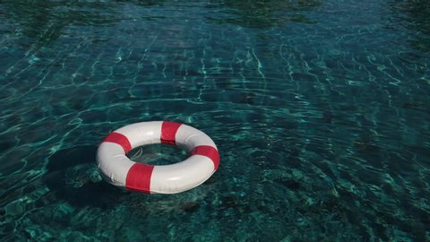 Lifebuoy Floating. Red life buoy over clear blue sea or ocean water background, swimming pool. Floating rescue buoy on the water surface. A floating lifebuoy. danger, 4 K slow-mo