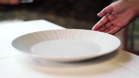 A waiter putting on the white plate on a table with a white table cloth