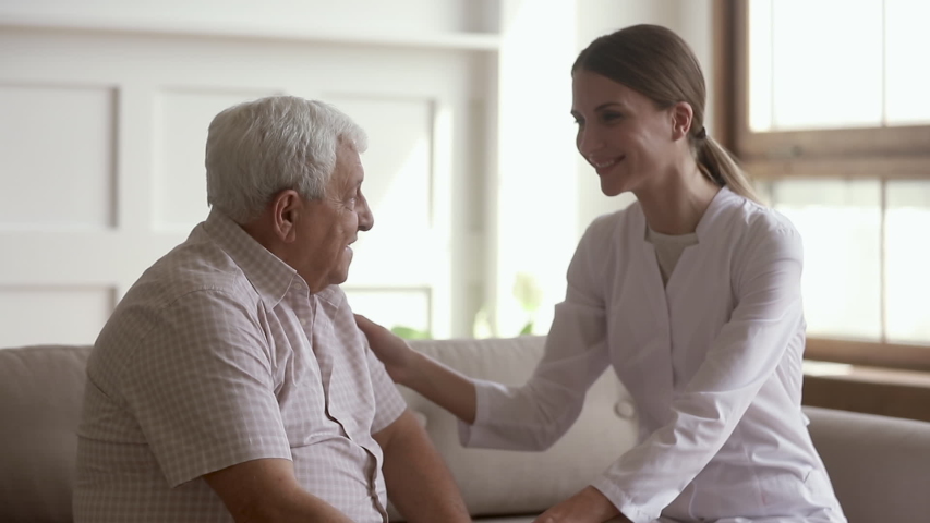Pleasant young female general practitioner visiting old retired patient at home, stroking arms, listening to complaints. Smiling doctor comforting pensioner during checkup, giving psychological help. | Shutterstock HD Video #1042185724