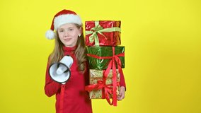 Girl in santa claus hat with box boxes in hand shouts into a megaphone, on a yellow studio background. Surprise. Emotions. 4K UHD Video