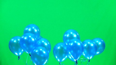 Balloons are pink then blue then white rises slowly on a green screen. Slow motion.