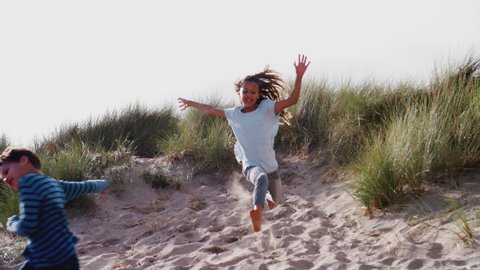Two Children Running And Jumping In Sand Dunes On Winter Beach Vacation