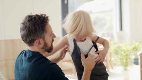 Young father helping small son to get dressed indoors in bedroom.