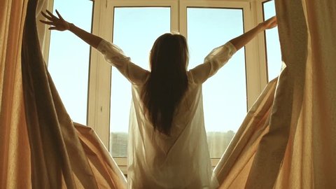 Woman in the morning. Attractive sexy woman with slender body opens curtains on big window and let the light in the room and has a perfect cozy morning. Slow motion