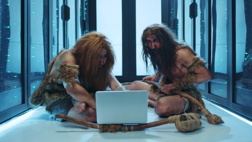 Primeval wild men of hunter-gatherers discovering technology inside futuristic data center. Prehistoric savages IT engineers using a laptop for maintenance in server cabinet. Royalty-Free Stock Footage #1042213000
