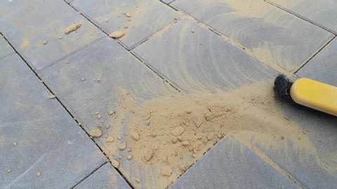 The final stage of laying paving slabs is the filling of gaps with dry sand. Female hand sweeps sand with a broom on a gray surface of concrete slabs
