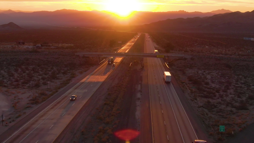 AERIAL, SUN FLARE: Cars and trucks cross the Mojave desert on a sunny summer morning. Big rig trucks and cars drive along the scenic highway running across the barren California landscape at sunset. Royalty-Free Stock Footage #1042216363