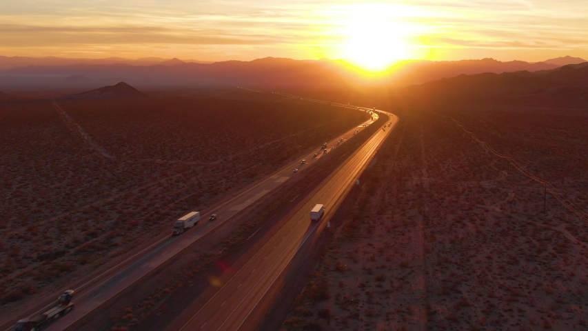 DRONE, LENS FLARE: Flying behind a freight truck driving along the Mojave freeway at sunrise. Freight trucks and cars move along the asphalt highway running across rural California on a sunny morning. Royalty-Free Stock Footage #1042216369