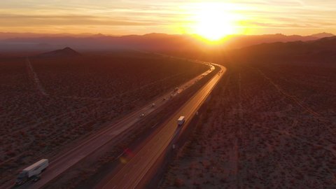 DRONE, LENS FLARE: Flying behind a freight truck driving along the Mojave freeway at sunrise. Freight trucks and cars move along the asphalt highway running across rural California on a sunny morning.