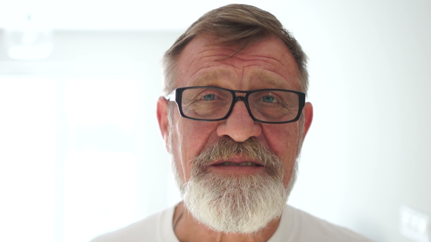 Happy kind grandfather with a gray beard smiles and masters at the camera. Elderly man, close portrait on a white background