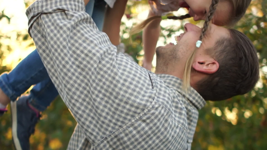Handsome young man lifts his little daughter in her arms with two pigtails. girl laughs cheerfully. Happy family in the apple orchard Royalty-Free Stock Footage #1042223665